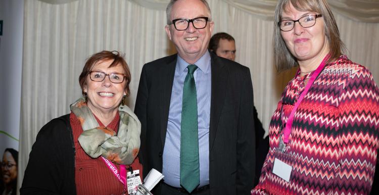 Two women and a man stood talking at an indoor event