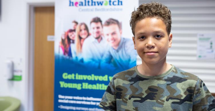 Young boy standing in front of a Healthwatch banner